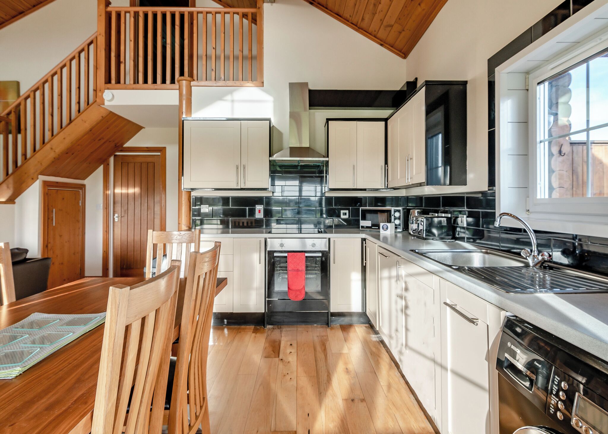 Eine moderne Küche mit Holzböden, einem Essbereich mit Holztisch und -stühlen sowie einer Treppe mit Holzwandungen.