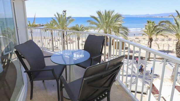 A balcony with a glass table and chairs, overlooking a beach with palm trees and the sea. - Comfortable Apartment in Salou Beachfront with Air Conditioning (Salou)