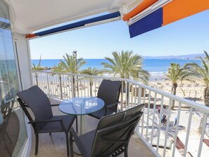 A balcony with a glass table and chairs, overlooking a beach with palm trees and the sea. - Comfortable Apartment in Salou Beachfront with Air Conditioning (Salou)
