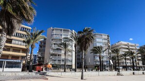 A beachfront hotel with multiple balconies, palm trees, and a sandy beach area. - Comfortable Apartment in Salou Beachfront with Air Conditioning (Salou)