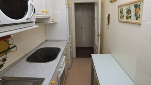 Cocina compacta con microondas, estufa y lavamanos. Hay una puerta que conduce a otra habitación.