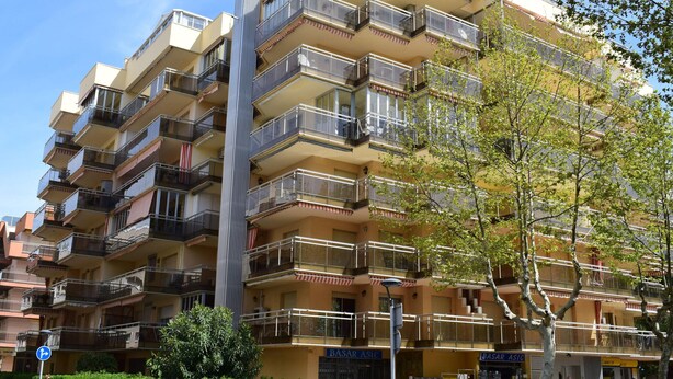 Un edificio residencial de varios pisos con balcones, vista a la calle y una tienda ASIC cercana.