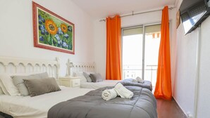 Habitación de hotel con dos camas, un cuadro de girasoles, cortinas anaranjadas y un televisor en la pared.