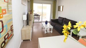 Una sala de estar con sofá, una mesa de centro, un mueble para televisión y un cuadro en la pared.