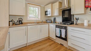A modern kitchen with white cabinetry, a stainless steel stove, and a microwave. - Lakeview 3 Pet Friendly (Woodhall Spa)