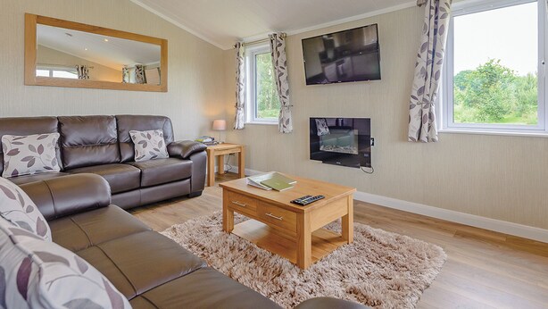 A living room with a sofa, a coffee table, a TV, and a window with curtains. - Lakeview 3 Pet Friendly (Woodhall Spa)