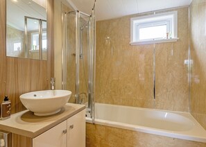 A bathroom with a large white sink, a glass-enclosed shower, a bathtub, and a window above the bathtub.