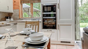 Una cocina moderna con horno y microondas integrados, una mesa de comedor dispuesta con platos y cubiertos, y un ventanal con vistas a zonas verdes.