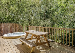 A wooden deck with a hot tub and picnic table surrounded by dense greenery.