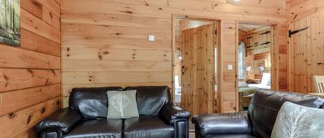 A wooden cabin interior with a leather sofa, a wooden table, and a door leading to another room.