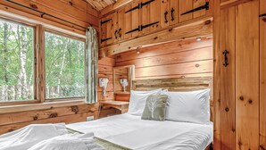 Un dormitorio de cabaña de madera con cama, mesita de noche, espejo y ventana.