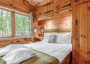 Un dormitorio de cabaña de madera con cama, mesita de noche, espejo y ventana.
