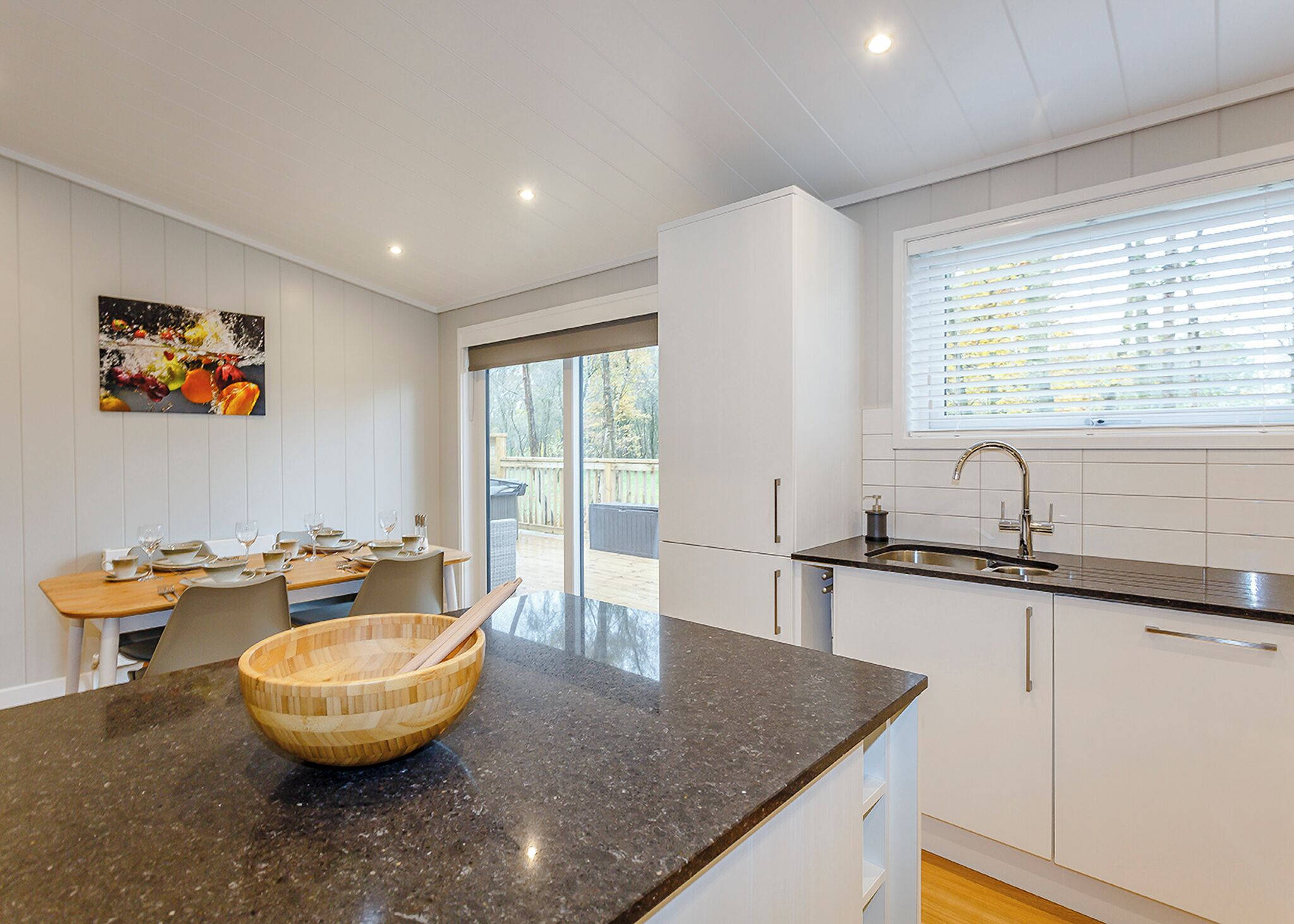 A modern kitchen with a granite countertop, wooden bowl, and a dining area with a table set for four.