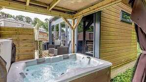 A hot tub in a covered outdoor area with wooden walls and a view of the surrounding neighborhood.