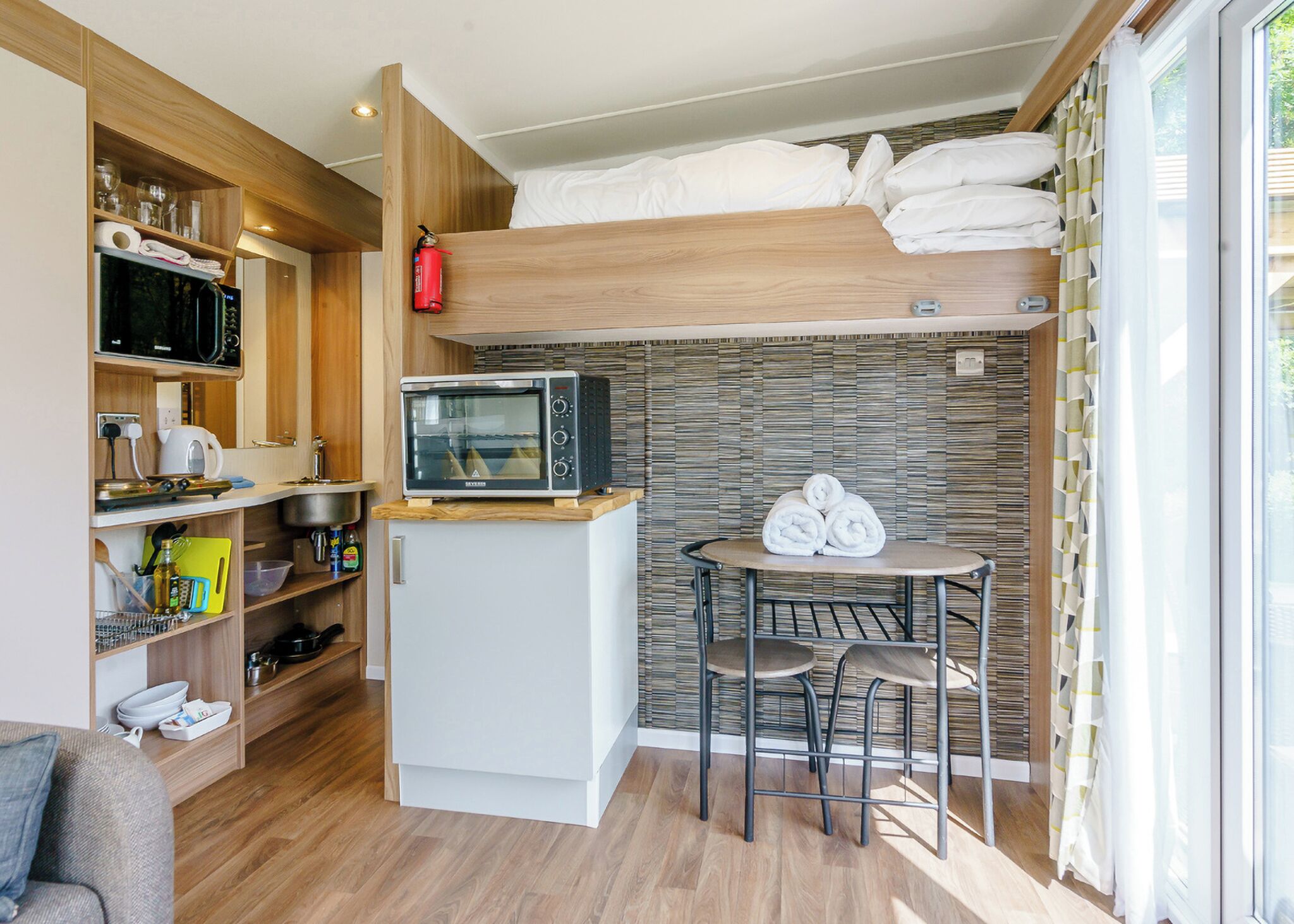 A compact kitchenette with a microwave, a small refrigerator, and a wooden shelf with kitchenware.