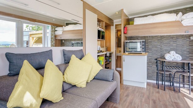 A compact RV interior with a sofa, a kitchenette, and a dining area.