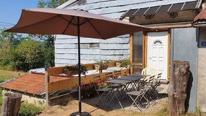 Una casa de madera rústica con un patio que cuenta con una mesa, sillas, un banco de madera y un gran paraguas.