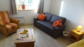 Un salón acogedor con un sofá, una mesa de centro de madera, una silla y una mesita de noche con una lámpara.