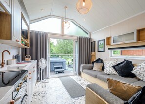 A modern kitchen with a stove, sink, and fan, a living area with a sofa and cushions, and a hot tub outside.
