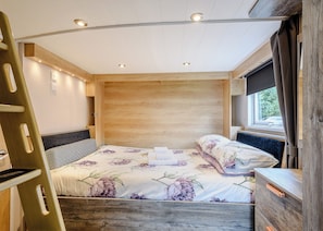 A bedroom with a bed, wooden headboard, and a window with curtains. - 1 bedroom accommodation in Newcastleton, (Newcastleton,)