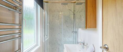 A modern bathroom with a glass shower enclosure, a white sink, and a towel rack.