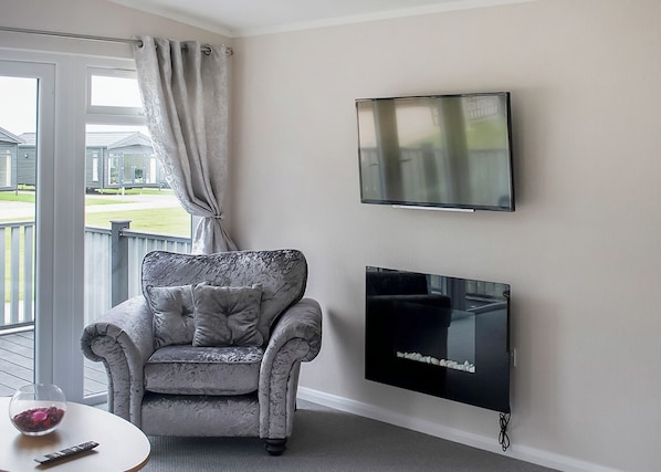 A living room with a grey armchair, a flat-screen TV, and a glass coffee table.