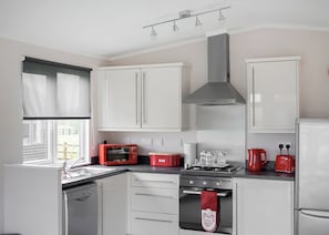 Une cuisine moderne avec des meubles blancs, un grille-pain rouge, une cuisinière à gaz et une hotte en acier inoxydable.