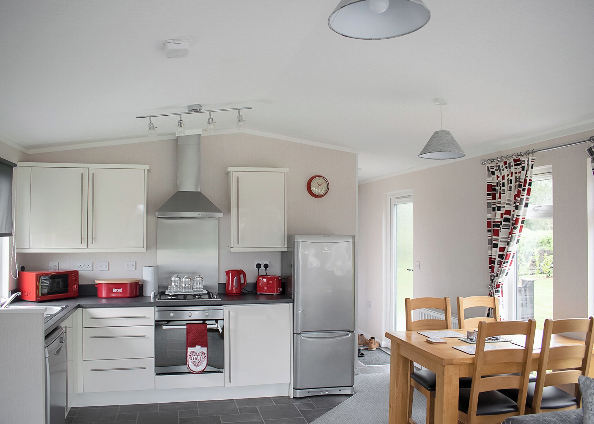 A kitchen with white cabinets, a red microwave, a gas stove, a refrigerator, and a dining area with wooden chairs.