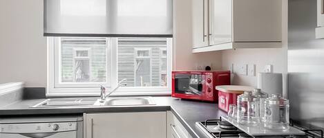 A kitchen with a window, a red microwave, a stove, and a dishwasher.