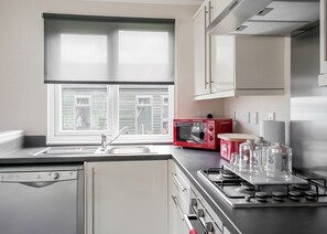 Une cuisine avec une fenêtre, un four à micro-ondes rouge, une cuisinière et un lave-vaisselle.