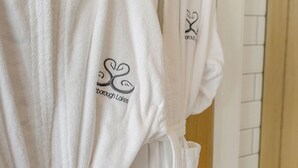 Une rangée de peignoirs blancs, ornés de motifs brodés et d’un cœur, est suspendue à un portant.
