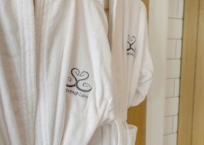 A row of white bathrobes with embroidered text and a heart design, hanging on a rack. - Woodland View Retreat (Lewes)