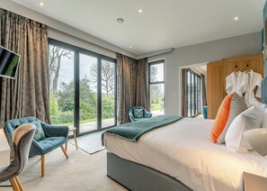 A modern hotel room with a large bed, two armchairs, a TV, and a view of the outdoors. - Woodland View Retreat (Lewes)