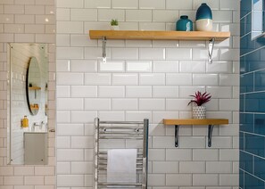 A bathroom with white subway tiles, a towel rack, a mirror, and two shelves with decorative items. - Woodland View Retreat (Lewes)