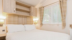 Ein Schlafzimmer mit Bett, Holzschrank, Nachttischlampen und einem Fenster mit Vorhängen.