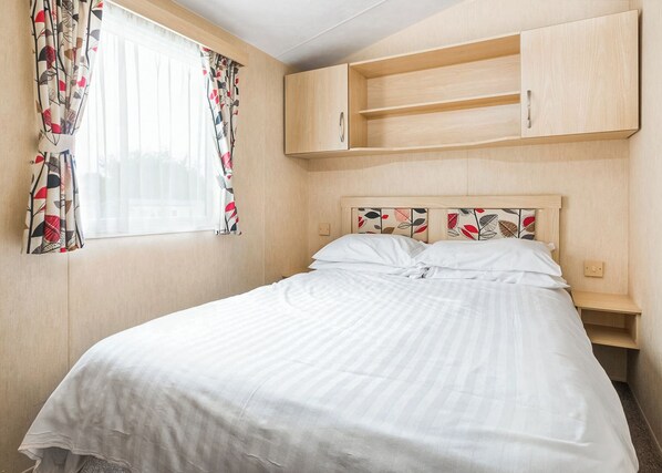 A bedroom with a bed, a window with curtains, and a wooden headboard with shelves.