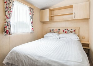 A bedroom with a bed, a window with curtains, and a wooden headboard with shelves.