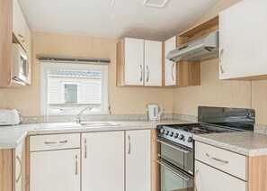 Una cocina compacta con estufa, horno, lavamanos y armarios.