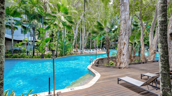 A pool surrounded by palm trees and lounge chairs, with a wooden deck and a sign indicating a no swimming zone.