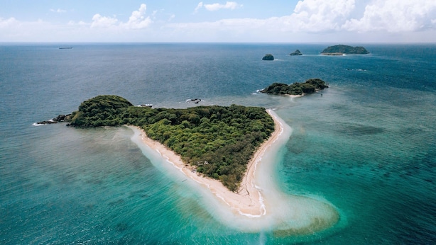 Vista aérea de una isla tropical con una playa arenosa estrecha y vegetación densa.