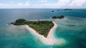 An aerial view of a tropical island with a narrow sandy beach and dense greenery.