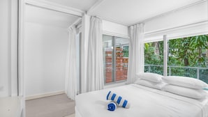 Habitación de hotel con una cama grande, cortinas blancas y vistas a zonas verdes, además de una puerta corrediza de vidrio.