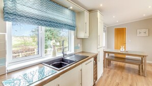A kitchen with a window, sink, and a dining area with a table and bench. - Luxury modern 2 Bedroom Lodge. (Swinethorpe, Nr Lincoln)