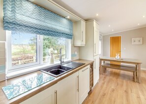 A kitchen with a window, sink, and a dining area with a table and bench. - Luxury modern 2 Bedroom Lodge. (Swinethorpe, Nr Lincoln)
