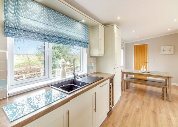 A kitchen with a window, sink, and a dining area with a table and bench. - Luxury modern 2 Bedroom Lodge. (Swinethorpe, Nr Lincoln)
