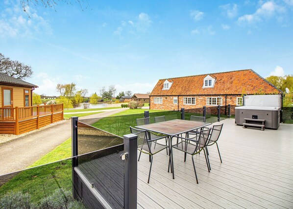 A wooden deck with a table and chairs, a hot tub, and a brick building with a tiled roof.