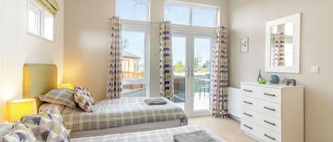 A bedroom with two beds, a dresser, a mirror, and a view through a glass door.