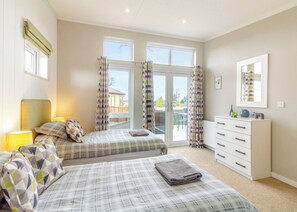 A bedroom with two beds, a dresser, a mirror, and a view through a glass door.
