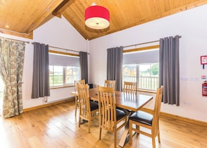 A dining area with a wooden table and chairs, large windows with curtains, a red ceiling light, and a fire extinguisher on the wall. - Outstanding, spacious and contemporary two storey lodge. (Hornsea)