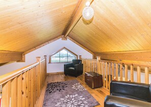 A wooden interior with a sloped ceiling, a window, a black leather sofa, a wooden chest, and a patterned rug. - Outstanding, spacious and contemporary two storey lodge. (Hornsea)